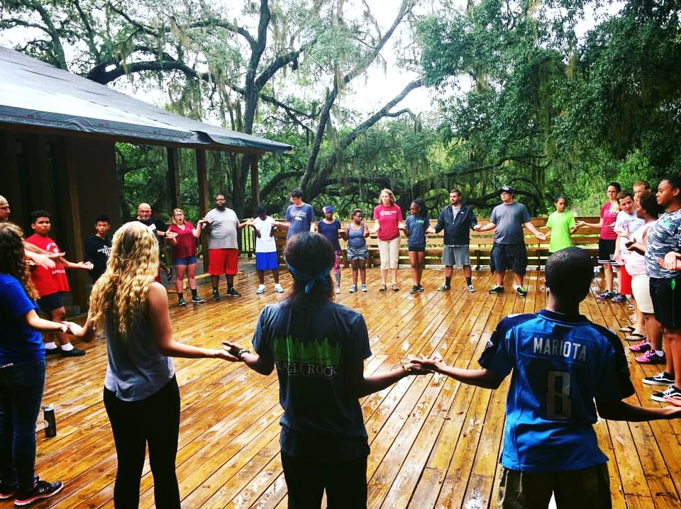 large group of people standing in a circle holding hands on an outdoor deck