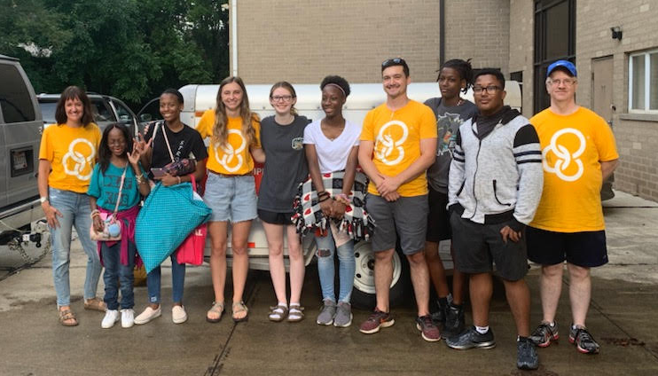 group of people adults and youth standing with luggage infront of a van